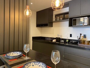 A modern kitchen with dark cabinetry, a stainless steel microwave, and a black countertop. - Bela Hospedagem - Mahalo Flats a 80m da praia (João Pessoa)