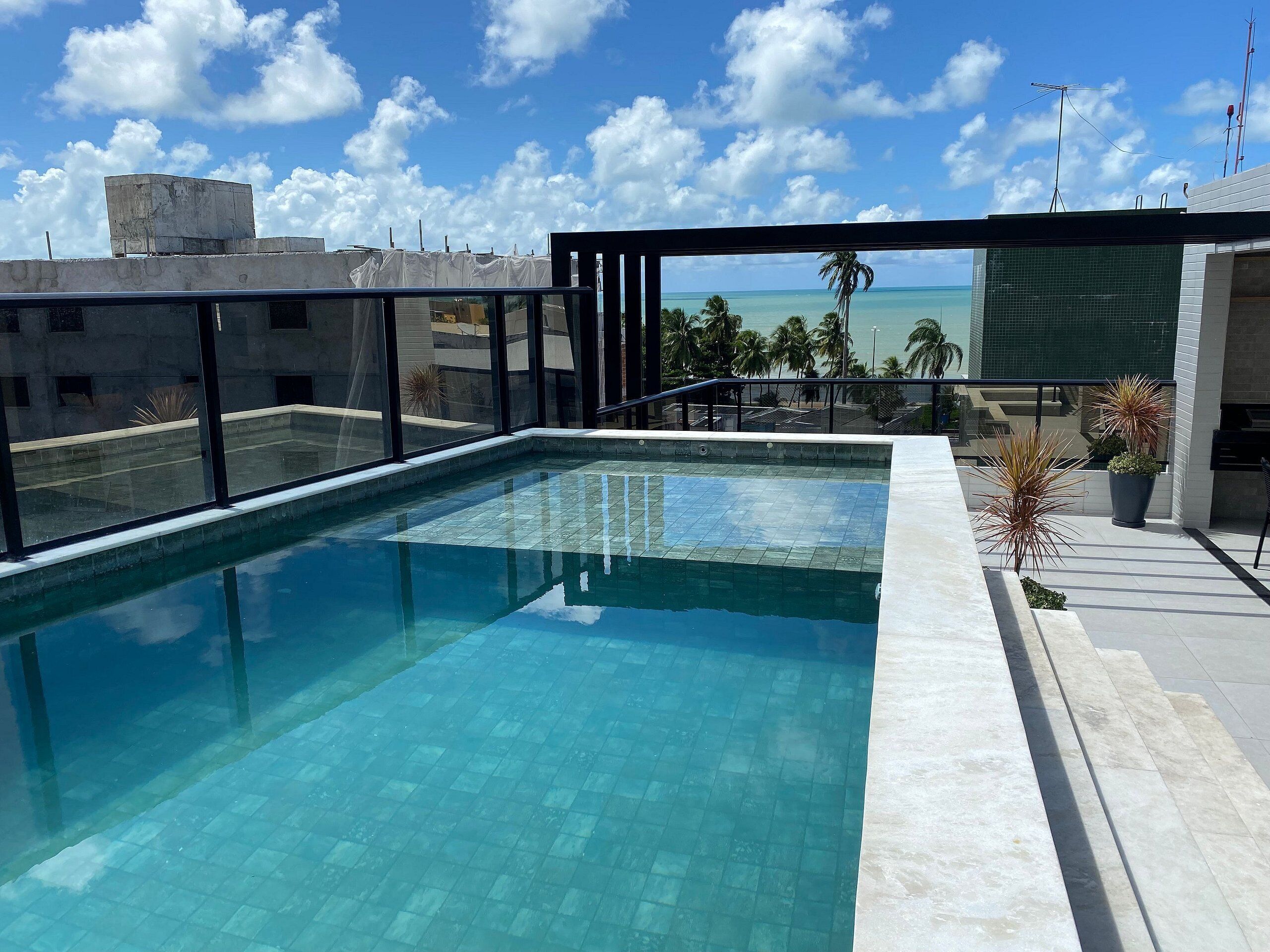 A rooftop swimming pool with a view of the ocean and palm trees.