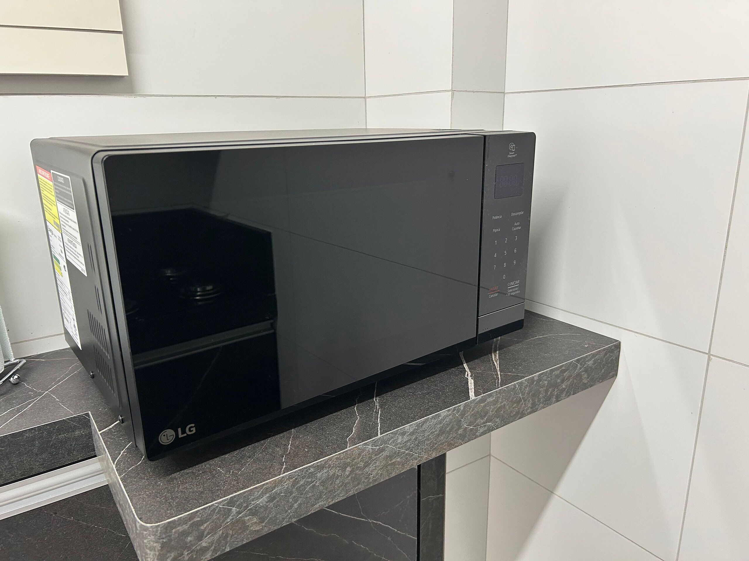 A black LG microwave oven on a marble countertop in a kitchen with white tiled walls.