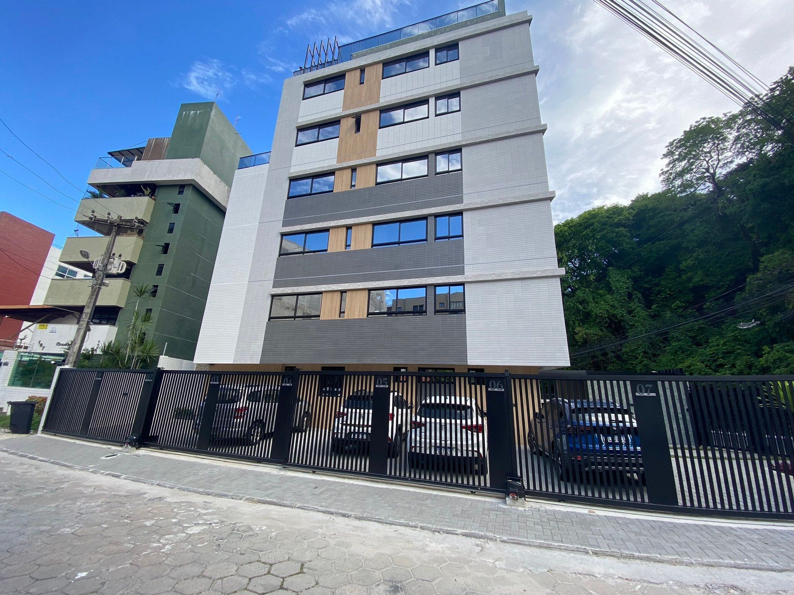 A multi-story building with a modern design, featuring a mix of glass and metal facade, and a gated parking area.
