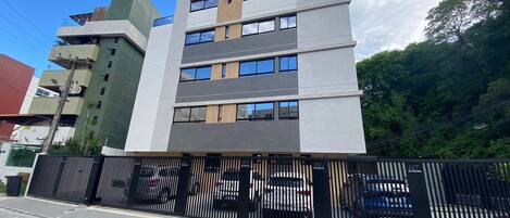A multi-story building with a modern design, featuring a mix of glass and metal facade, and a gated parking area.
