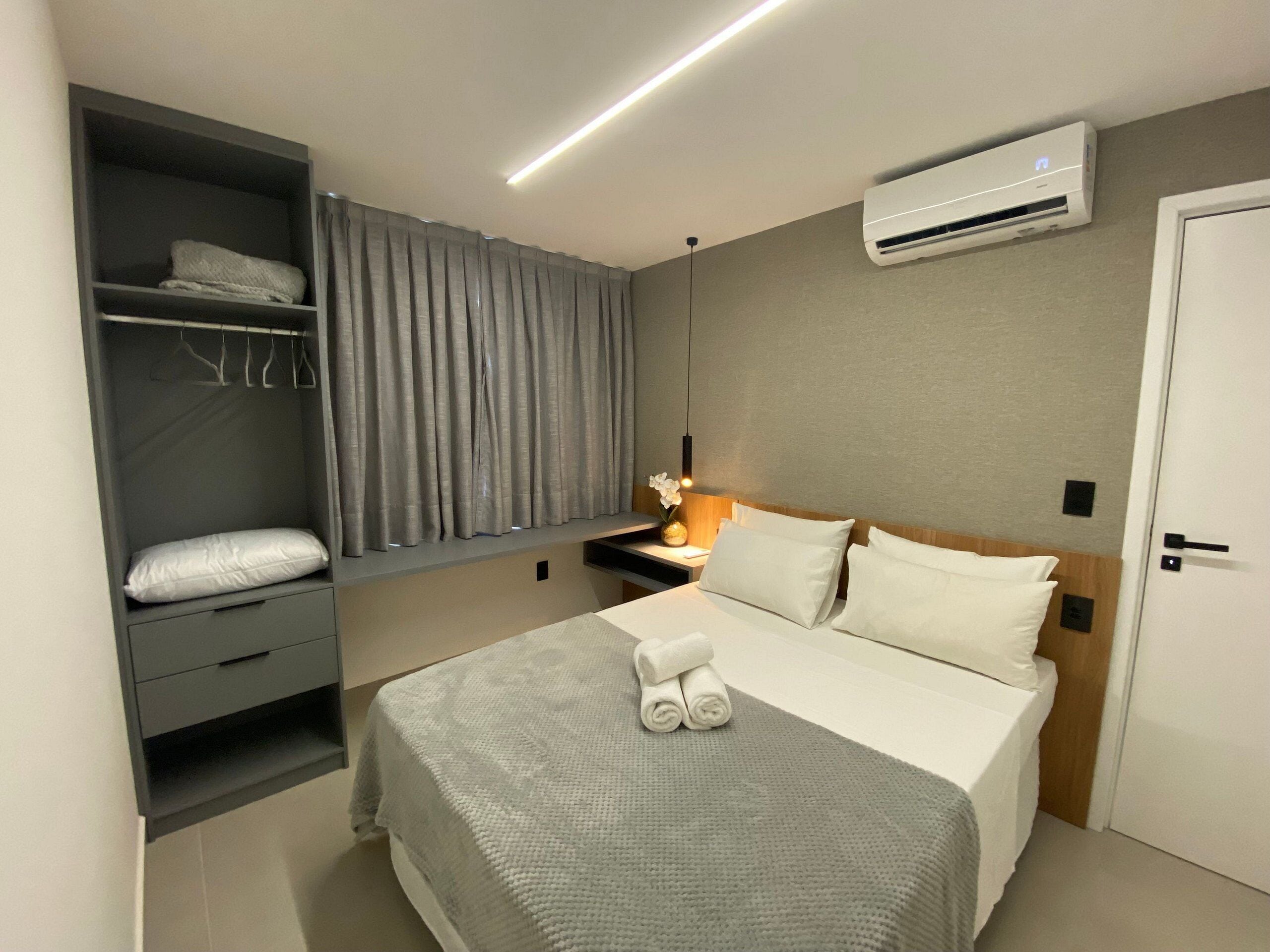 Een hotelkamer met een bed, een garderobe, een airconditioningsysteem en een nachtkastje met een lamp en vaas.