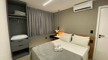 Een hotelkamer met een bed, een garderobe, een airconditioningsysteem en een nachtkastje met een lamp en vaas.