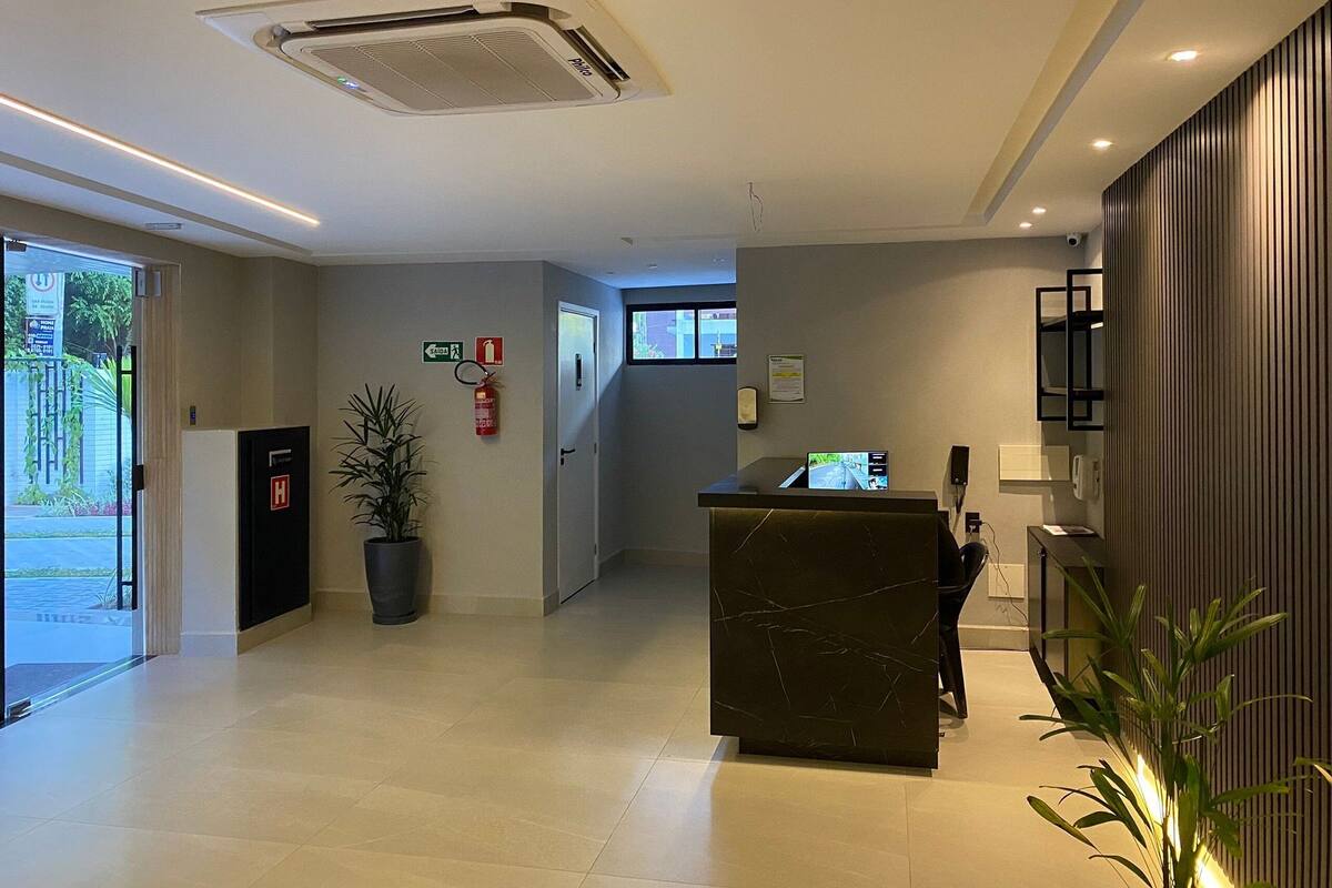 A hotel reception area with a reception desk, a fire extinguisher, a plant, and a fire exit sign.