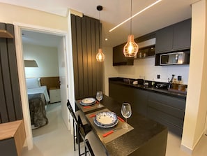 A modern kitchen with a central island, dark cabinetry, and pendant lighting. - Bela Hospedagem - Mahalo Flats a 80m da praia (João Pessoa)