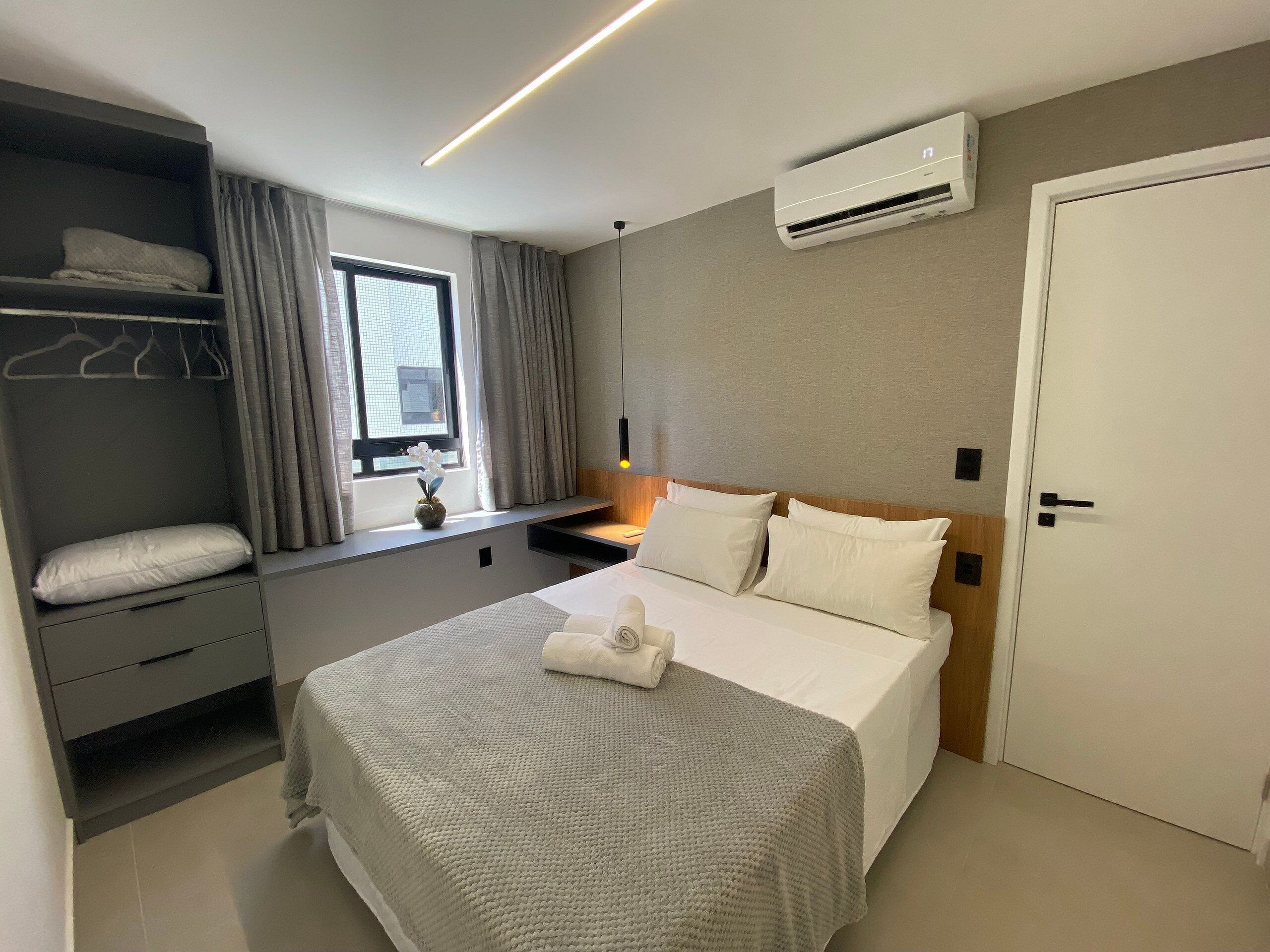 Une chambre d’hôtel comprenant un lit, une armoire, une fenêtre avec des rideaux, un appareil de climatisation et une porte.