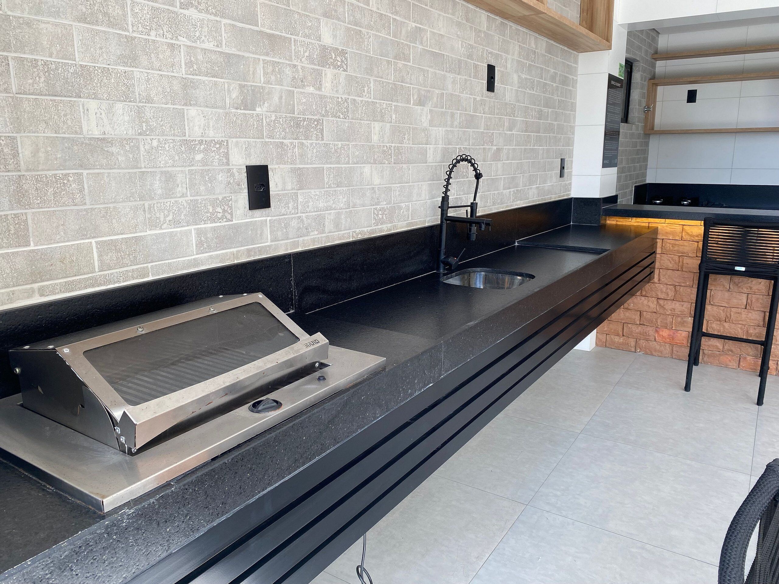 A kitchen with a brick backsplash, a stainless steel range hood, a black countertop, and a small brick accent wall.