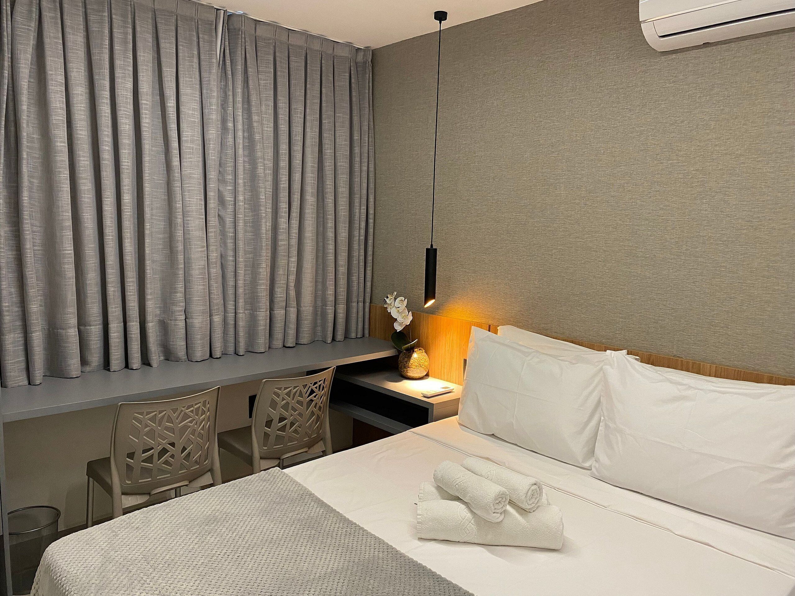 Une chambre d’hôtel équipée d’un lit, d’un bureau, d’une chaise, d’une table de chevet et d’un climatiseur fixé au mur.