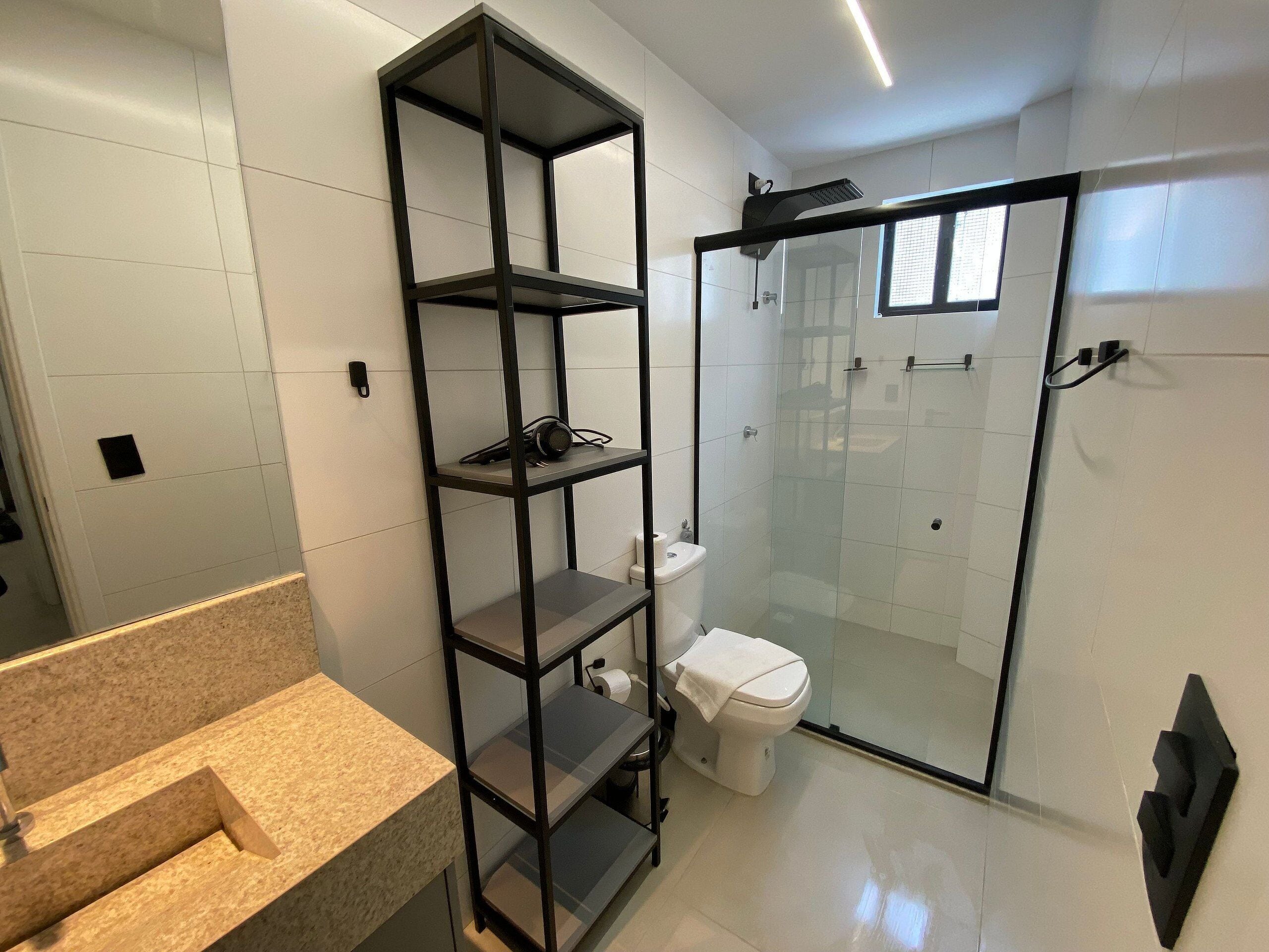 A modern bathroom with a glass shower enclosure, a built-in shelf unit, and a toilet.