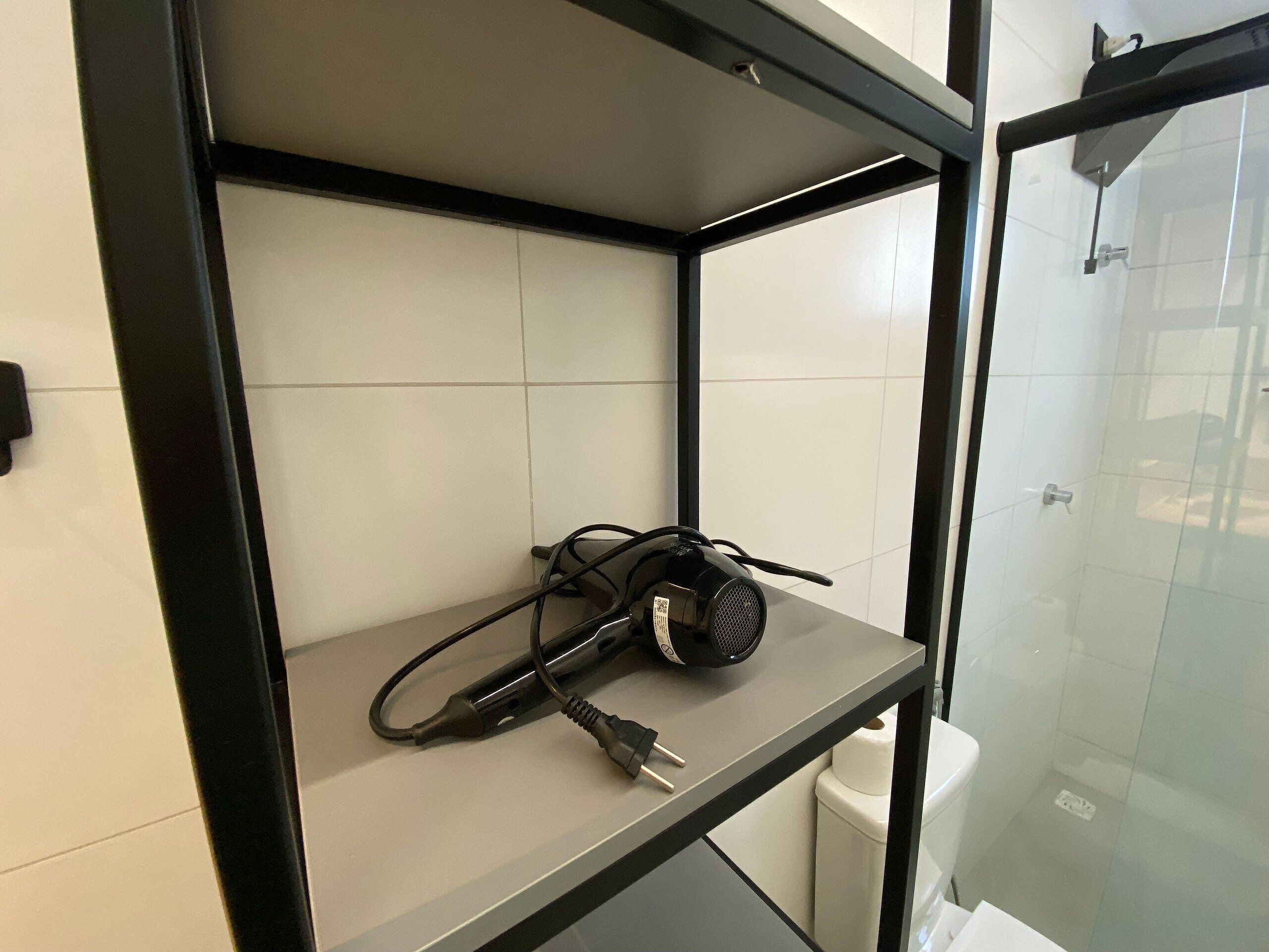 A bathroom with a shower, a toilet, and a shelf with a hairdryer.