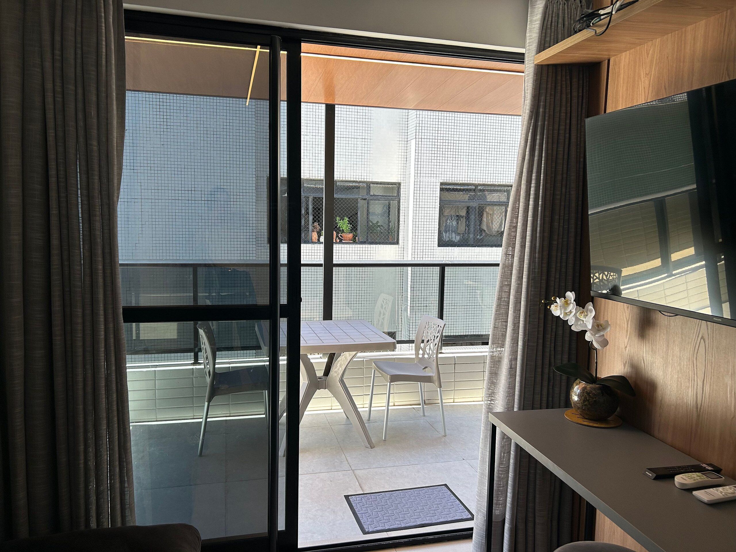 Une pièce dotée d’une porte-fenêtre coulissante donnant sur un balcon extérieur avec une table et des chaises.
