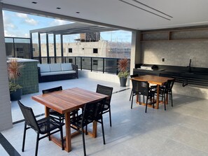 En moderne tagterrasse med spisebord, stole, sofa og et tekøkken.