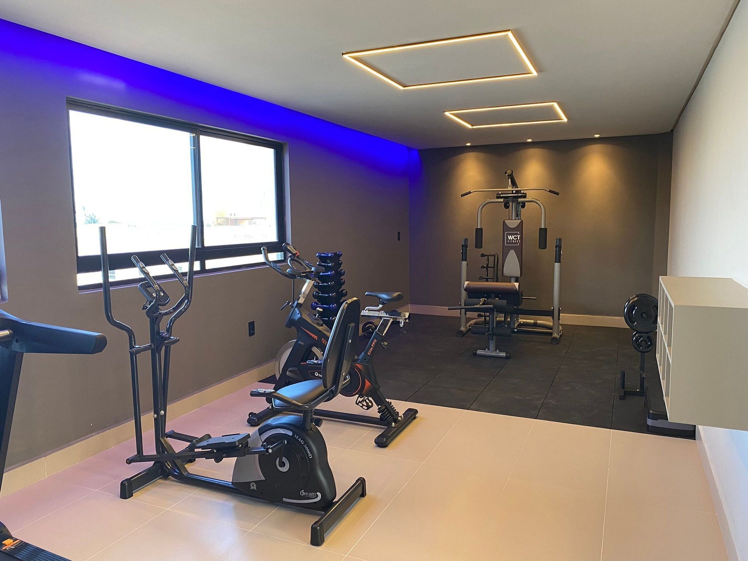A gym with exercise equipment, a large window, and modern lighting.