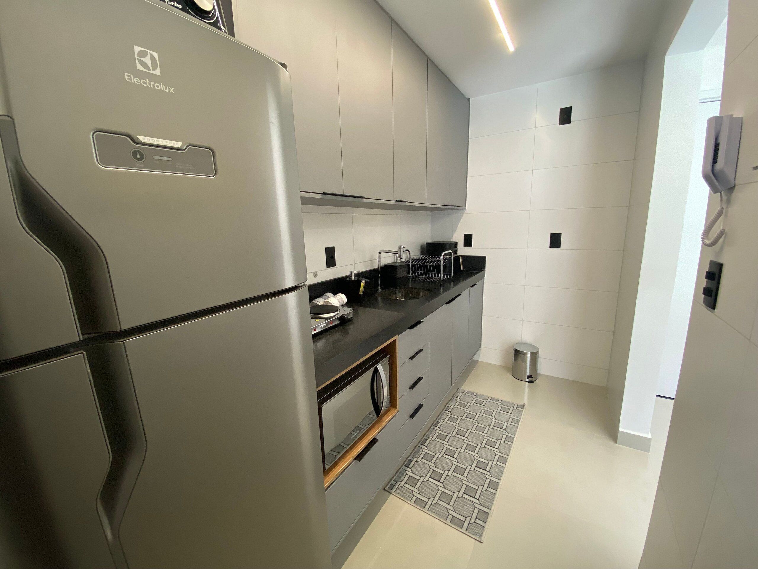 A modern kitchen with grey cabinets, a stainless steel refrigerator, a black countertop, and a patterned rug.