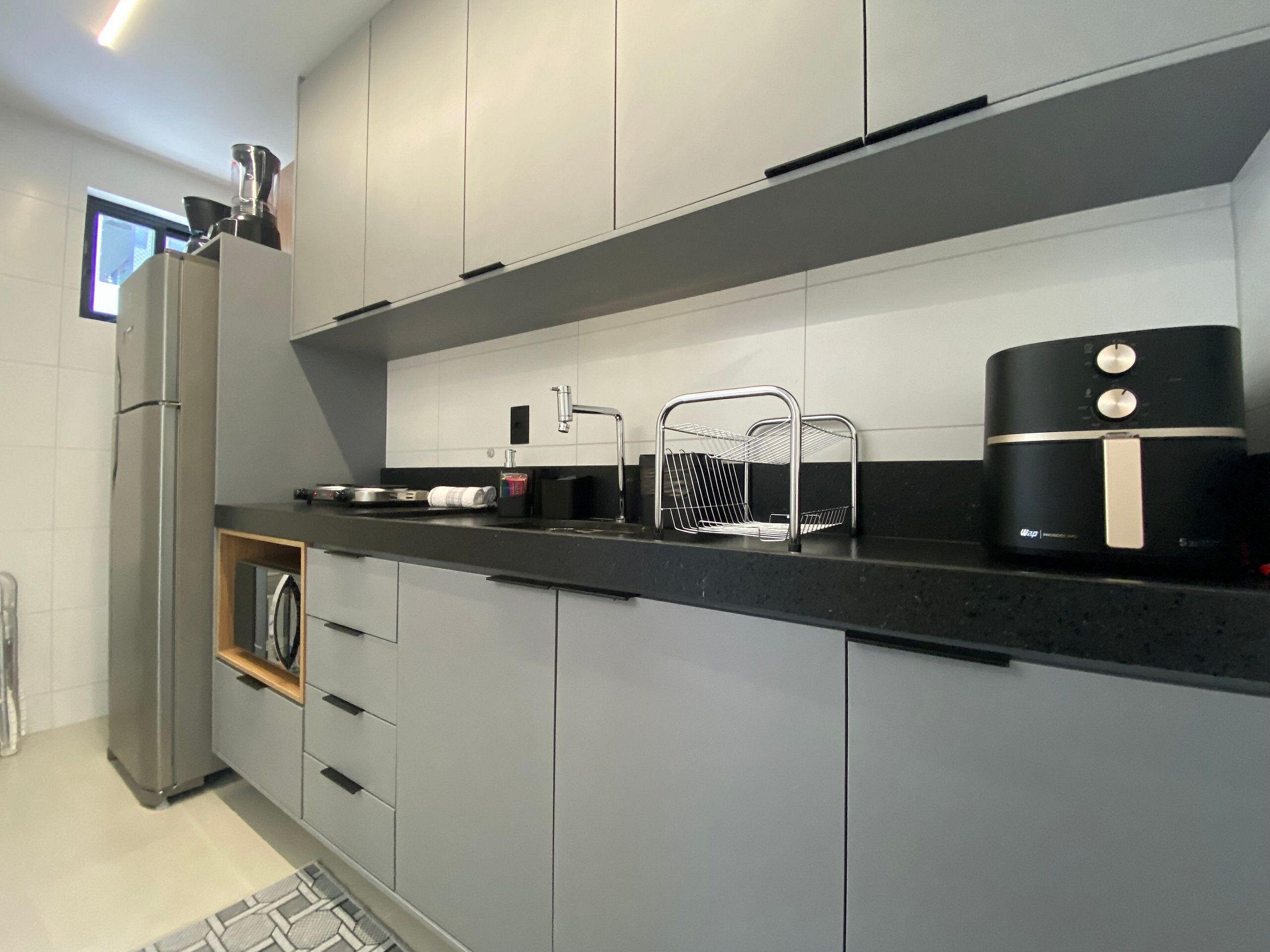 A modern kitchen with grey cabinets, a black countertop, a stainless steel refrigerator, a coffee maker, and a wire basket.