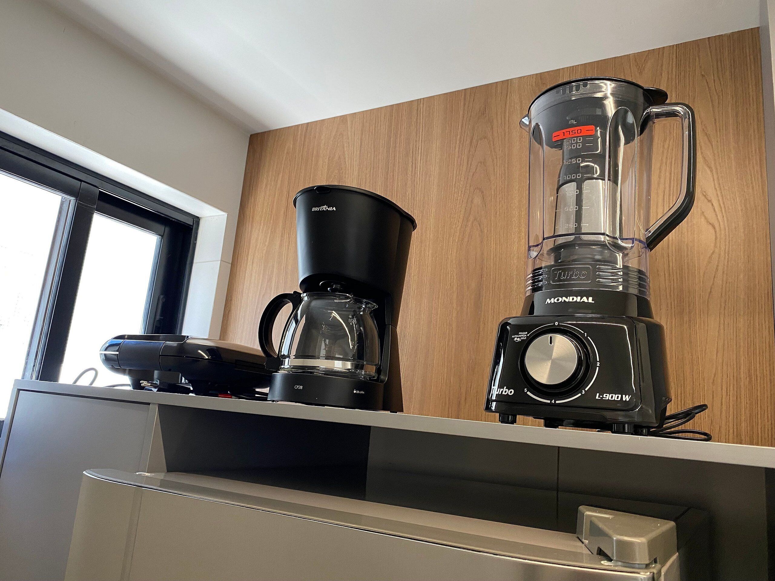 Uma cozinha com cafeteira, liquidificador e jarra de café em uma bancada de madeira.
