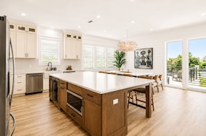 A modern kitchen with wooden cabinets, a large island, and a view to the outdoors. - Casa Blanca | Rooftop Bar • Elevator • Golf Cart • 400' Beach Access (Miramar Beach)