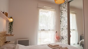 Ein Schlafzimmer mit einem Bett, einer Nachttischschublade, einer Hängeleuchte und einem Fenster mit Vorhängen.