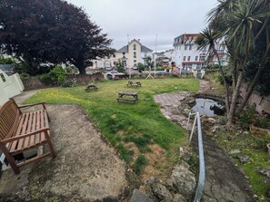 A backyard with a wooden bench, picnic tables, a small pond, and a grassy area with yellow flowers. - The Great Western Hotel (Paignton)