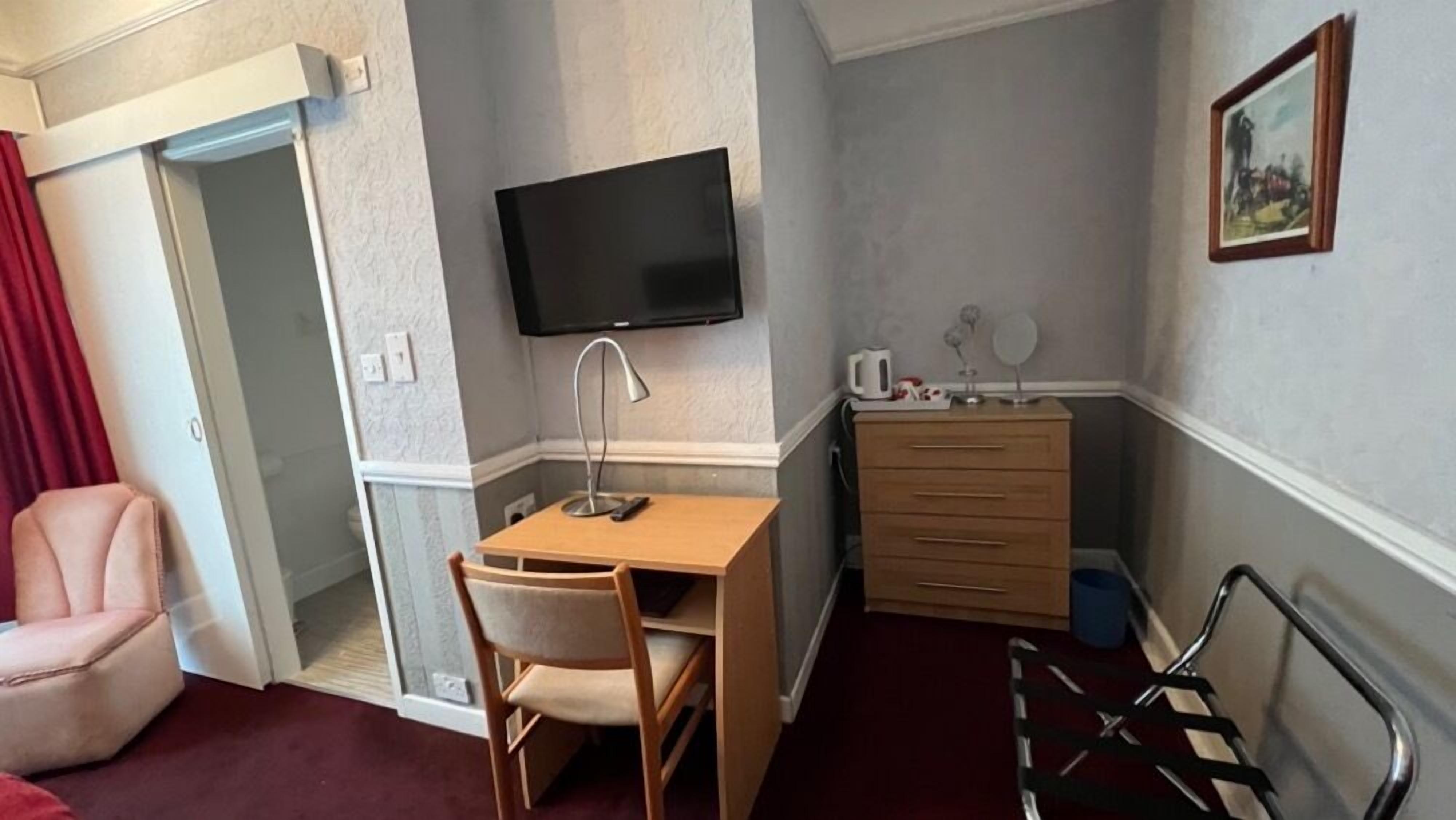 A compact hotel room with a desk, chair, television, and a small dresser.