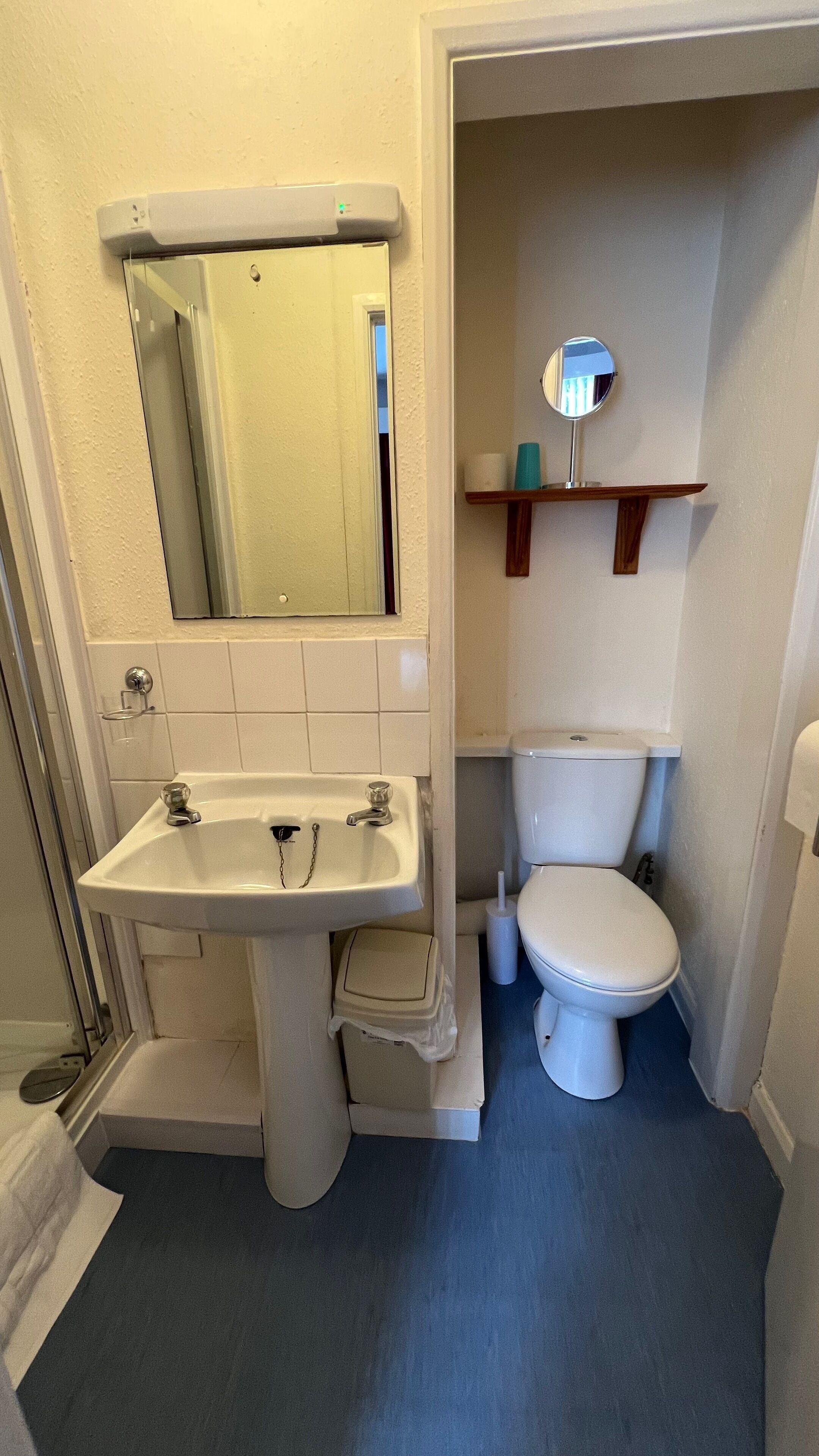 A bathroom with a sink, mirror, toilet, and a shelf with toiletries.