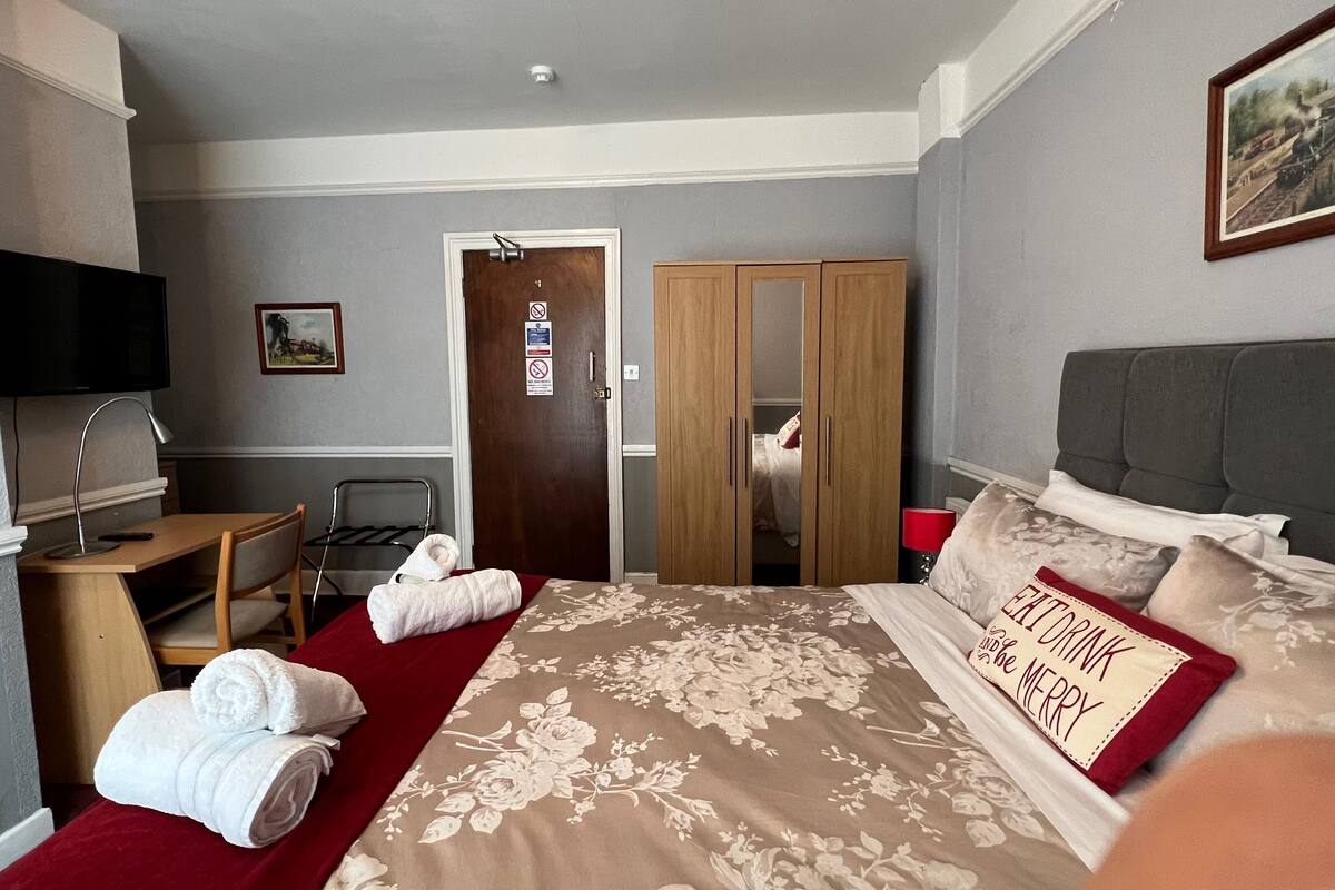 A hotel room with a bed, a desk, a chair, a TV, a wardrobe, and a door.