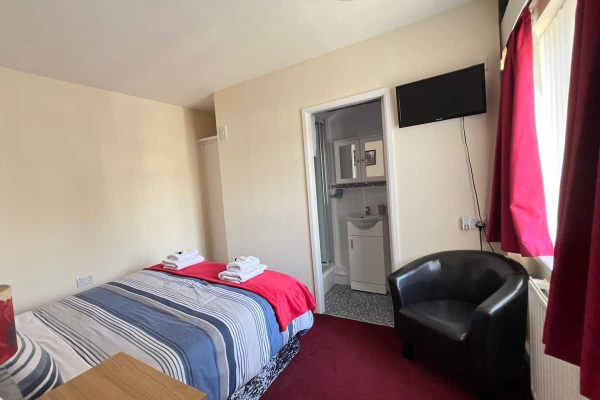 A hotel room with a bed, a chair, a TV, and a bathroom visible through an open door.