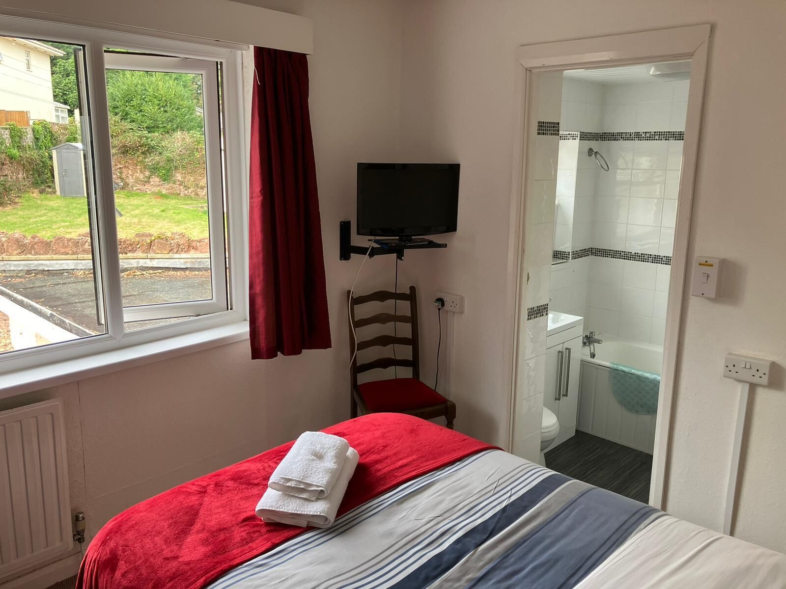 A bedroom with a bed, a TV, a chair, and a bathroom visible through an open door.