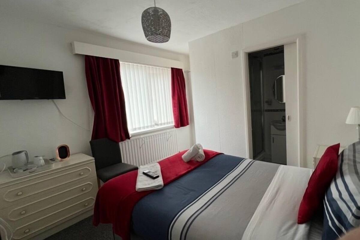 A hotel room with a bed, a dresser, a TV mounted on the wall, and a door leading to a bathroom.