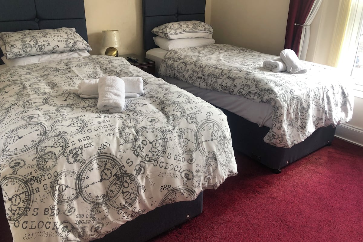 Two beds with matching bedding, a bedside lamp, and a window with curtains.