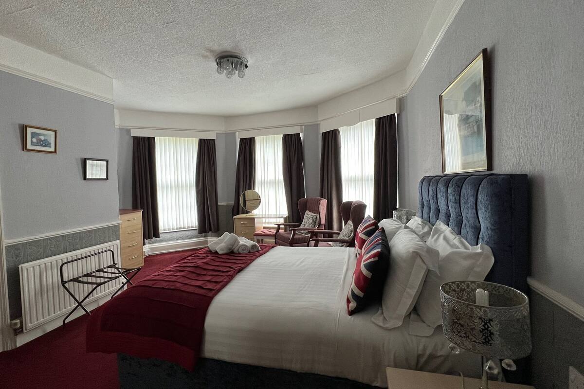 A hotel room with a neatly made bed, a chair, a desk, and a window with curtains.