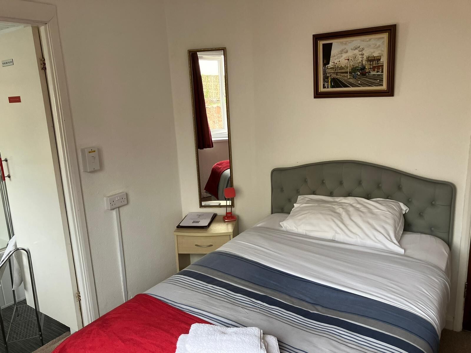 A hotel room with a bed, a bedside table, a mirror, and a painting on the wall.