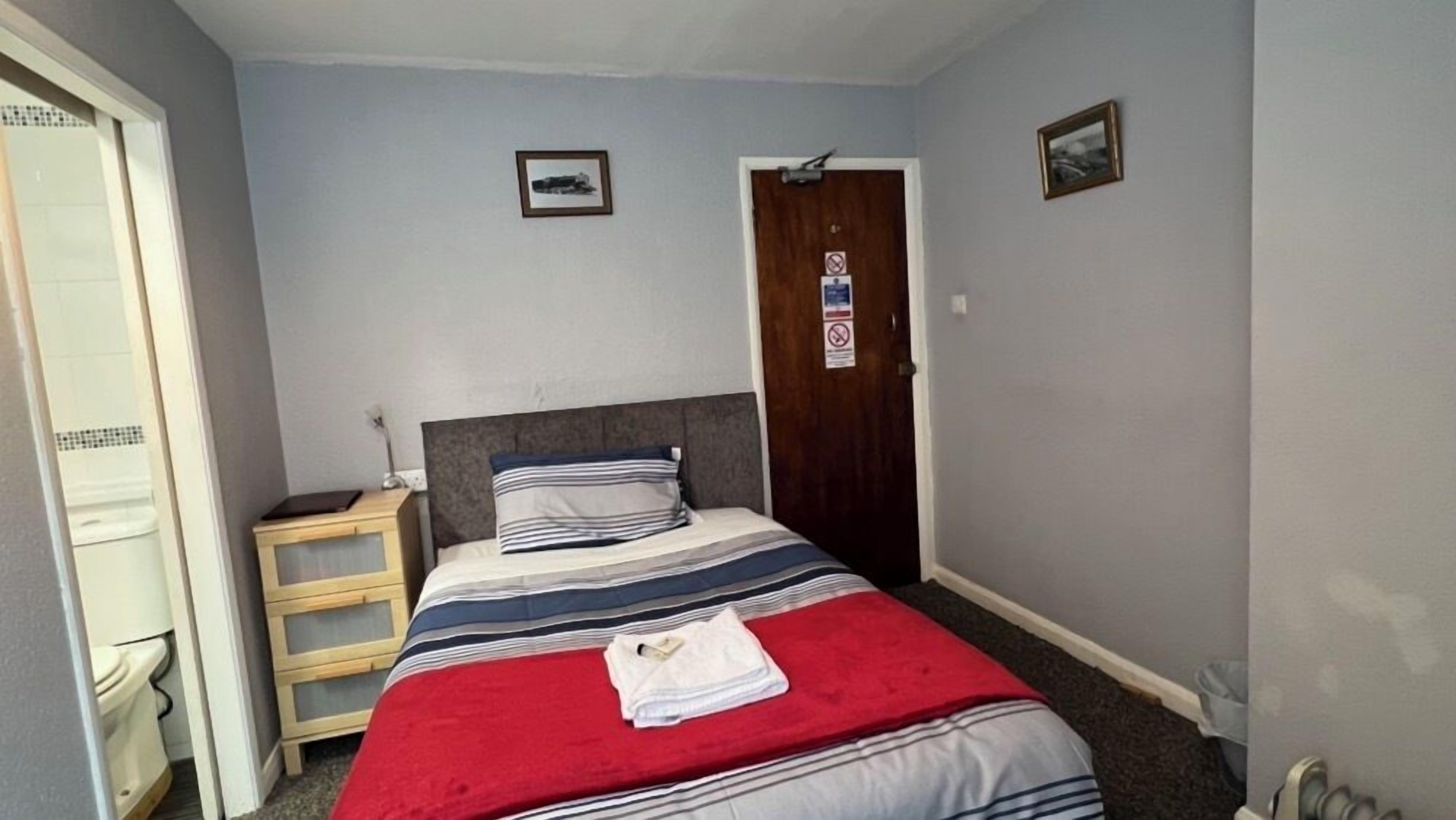 A bedroom with a bed, a wooden nightstand, a door, and a small picture on the wall.