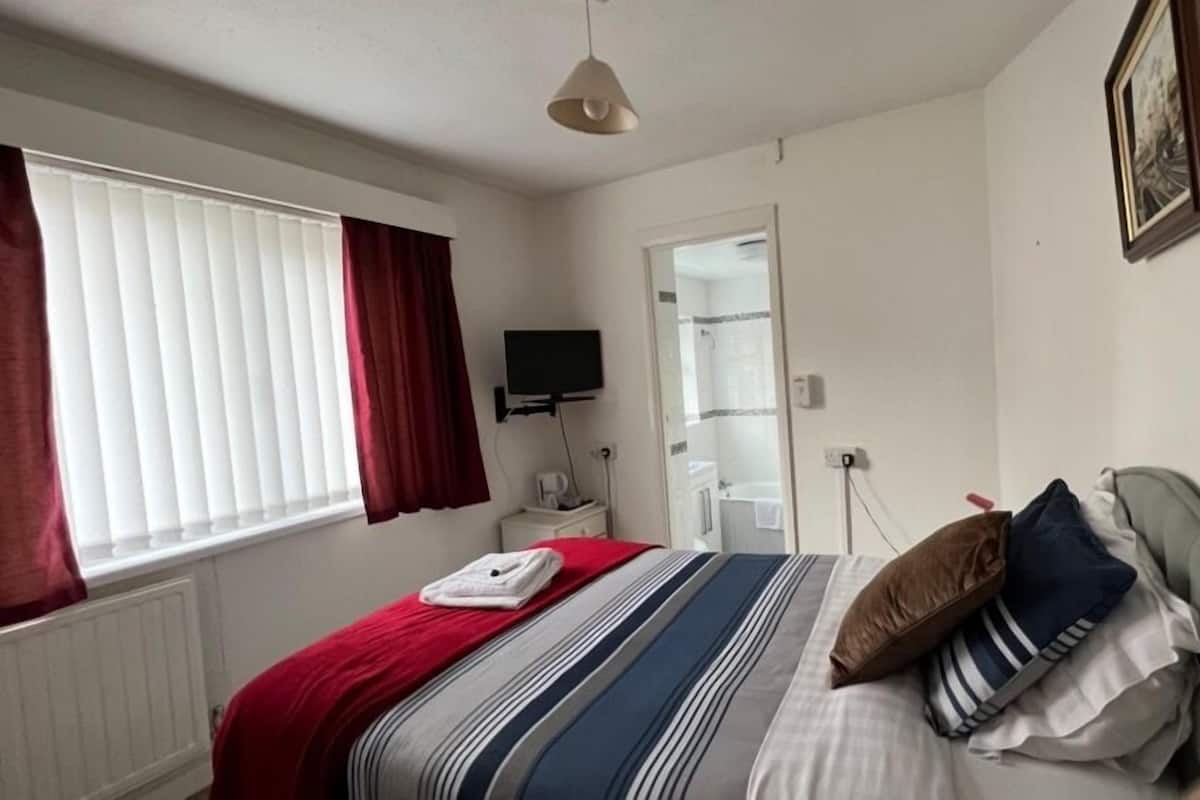 A hotel room with a bed, a television, a bathroom, and a window with curtains.