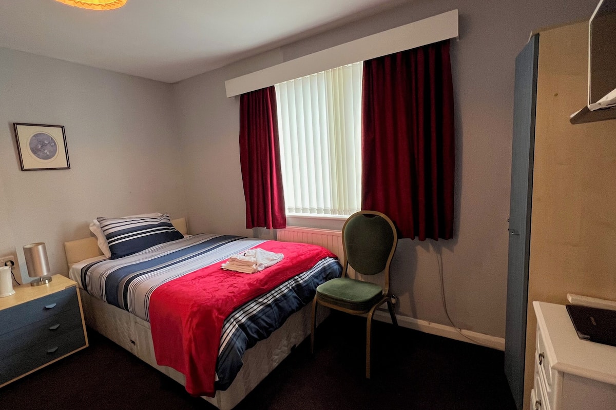 A bedroom with a bed, a chair, a desk, and a radiator.