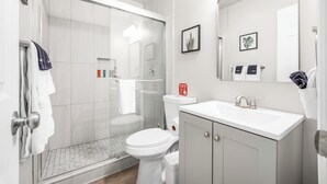 A modern bathroom with a glass-enclosed shower, a white toilet, and a vanity with a sink and mirror. - New Modern Apartment w/ AC - Central to SD (El Cajon)