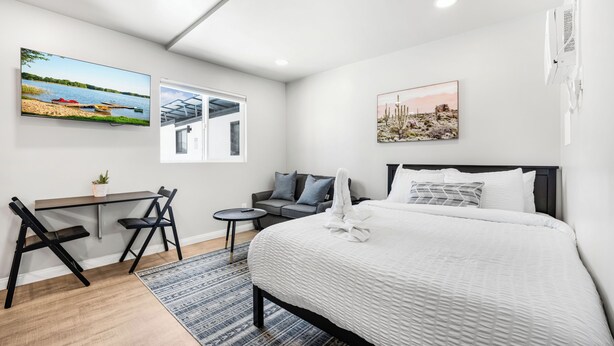 A modern hotel room with a large bed, a desk with chairs, a small sofa, and artwork on the walls. - New Modern Apartment w/ AC - Central to SD (El Cajon)