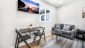A modern living room with a dining area, a gray sofa, and a TV mounted on the wall. - New Modern Apartment w/ AC - Central to SD (El Cajon)