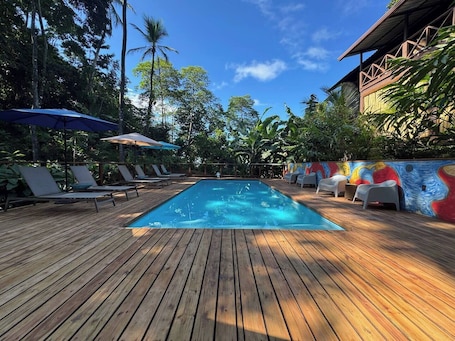 Una piscina al aire libre, sombrillas, sillones reclinables de piscina