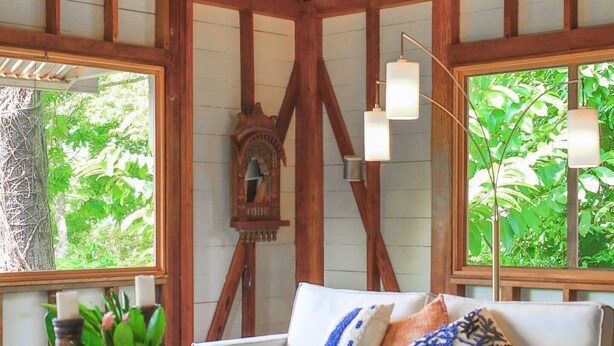 A cozy room with a wooden ceiling, a white sofa with decorative pillows, a wooden coffee table with a vase and flowers, and a blue and white patterned rug. - The Lodge at Punta Rica (Bastimentos)