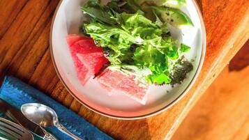 Une table en bois sur laquelle se trouve une assiette blanche contenant une salade, un verre d’eau et une cuillère, le tout posé sur une serviette bleue.