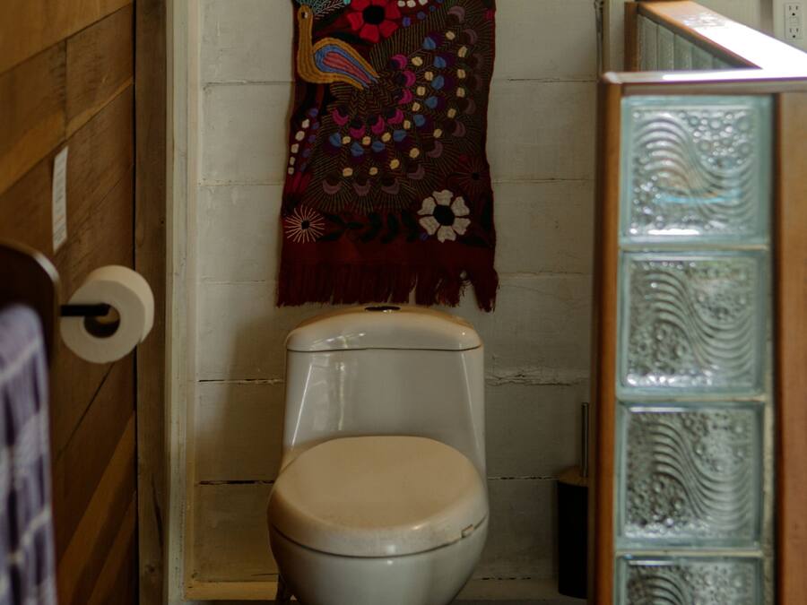 Un baño con un inodoro, una toalla colgada en la pared y una cortina de ducha estampada.