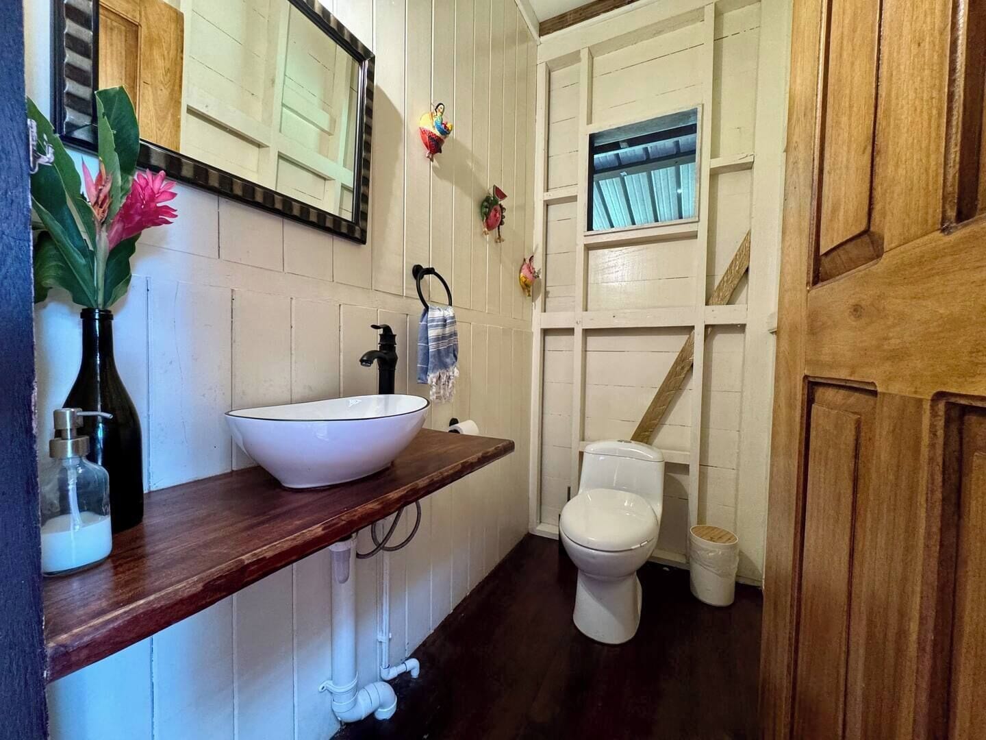 A bathroom with a white sink, black faucet, and a white toilet. There is a wooden door and a window with a curtain.