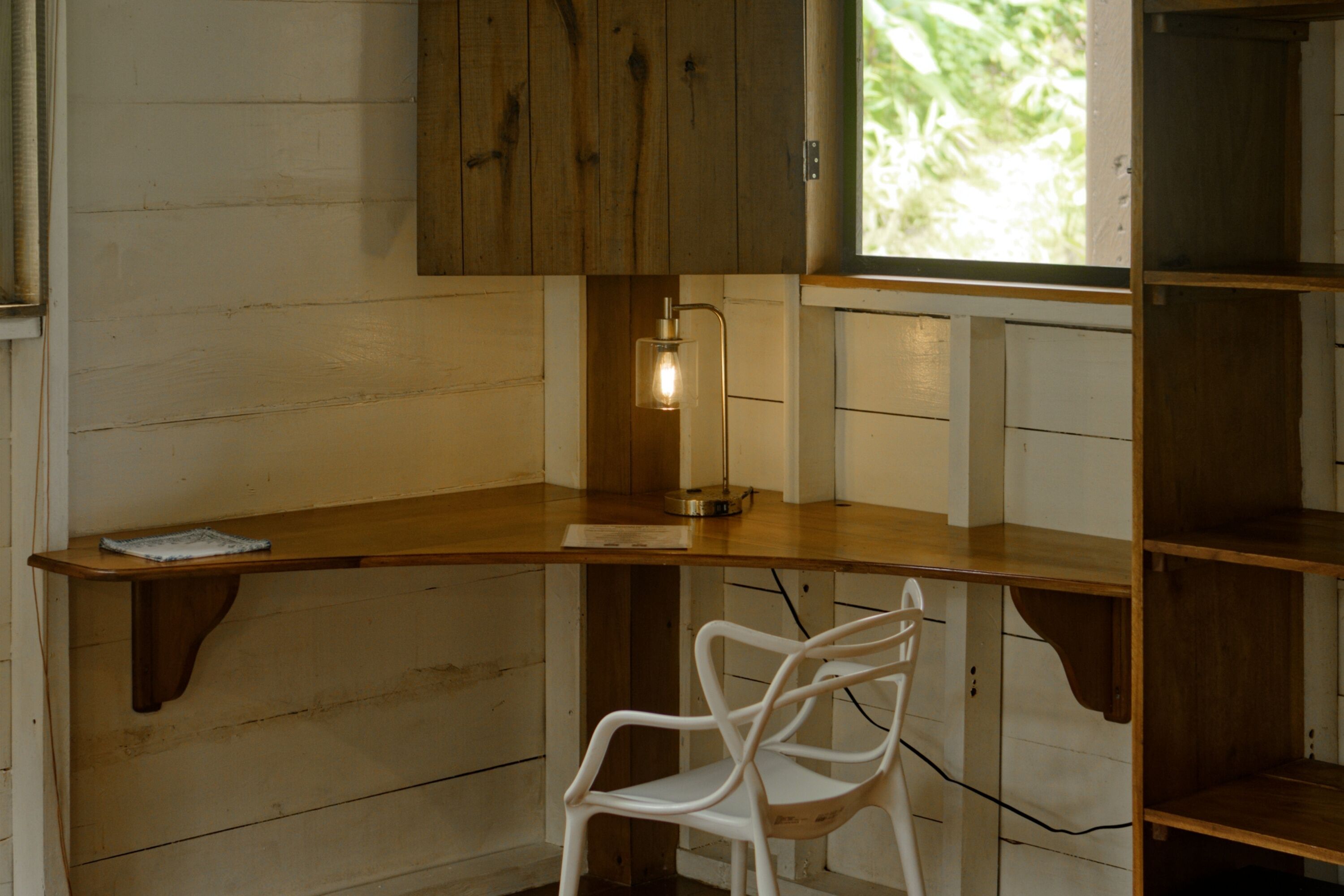 A corner workspace with a wooden desk, a white chair, and a pendant light.