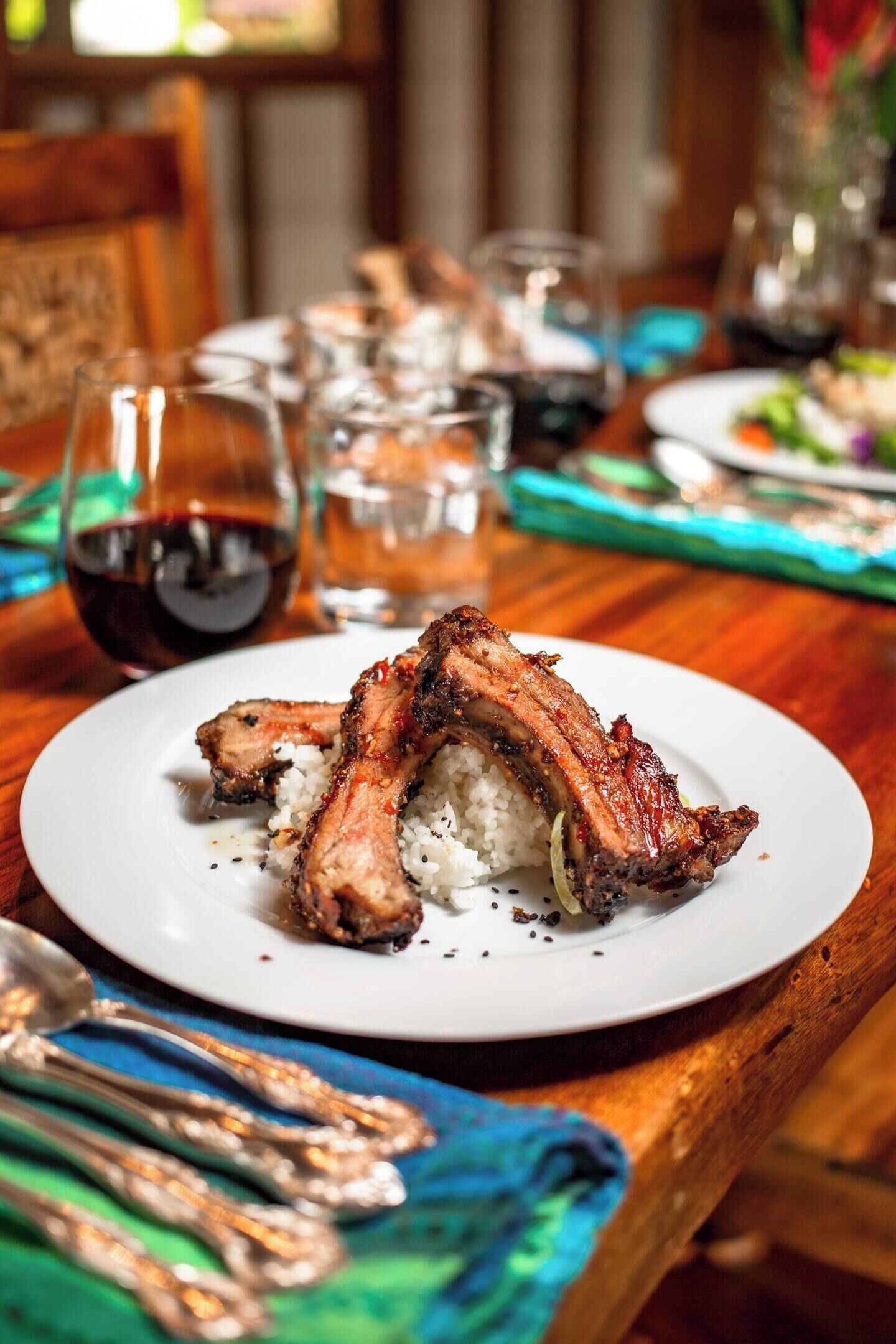 A plate of ribs with rice on a wooden table.