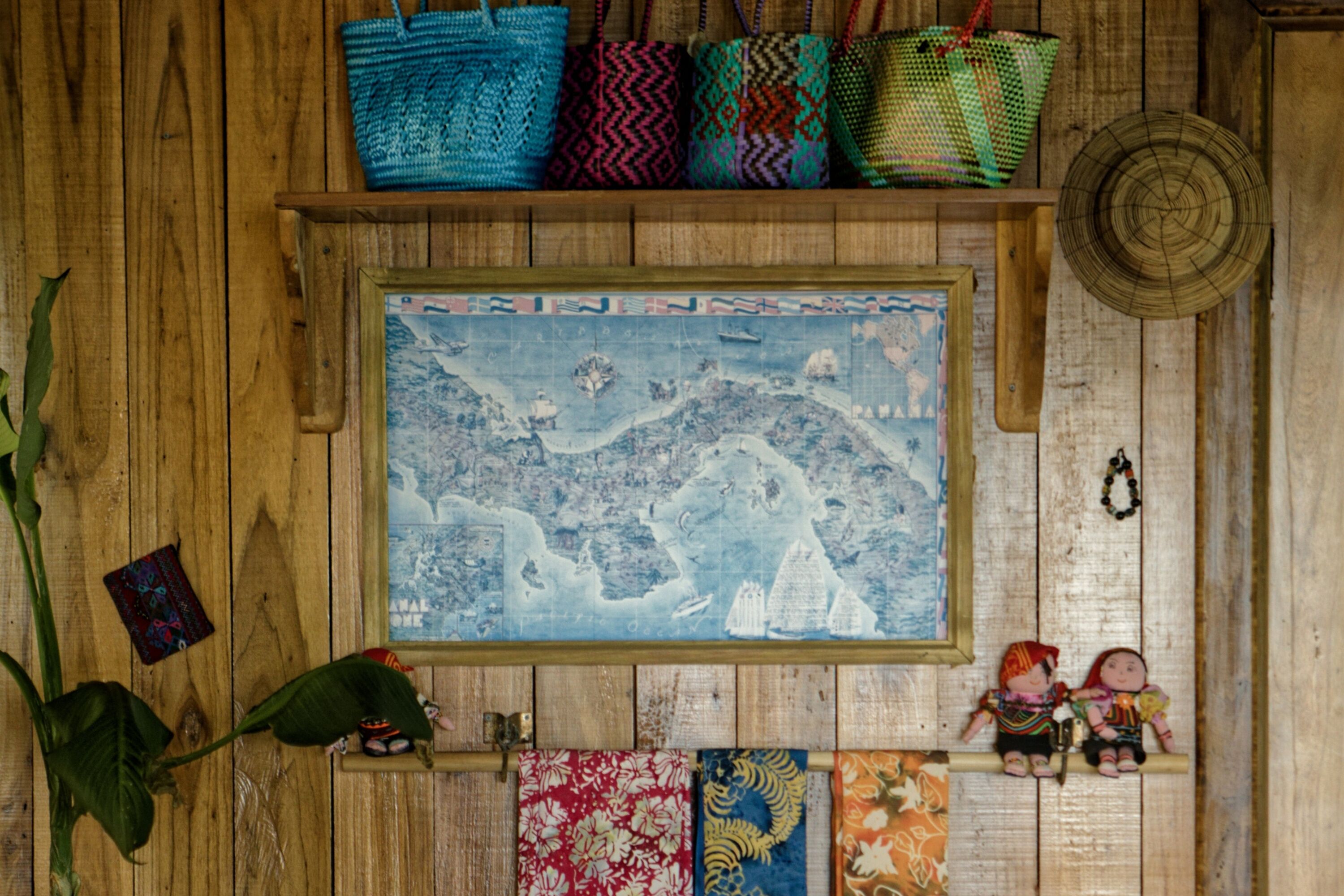 Pared de madera con un mapa enmarcado, una planta y un estante con bolsas de colores.
