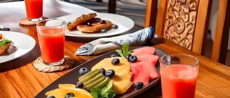 A breakfast setting with a fruit platter, croissants, and two glasses of red juice on a wooden table.