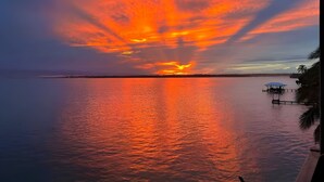 A sunset over a calm body of water with a dock and palm trees on the right.