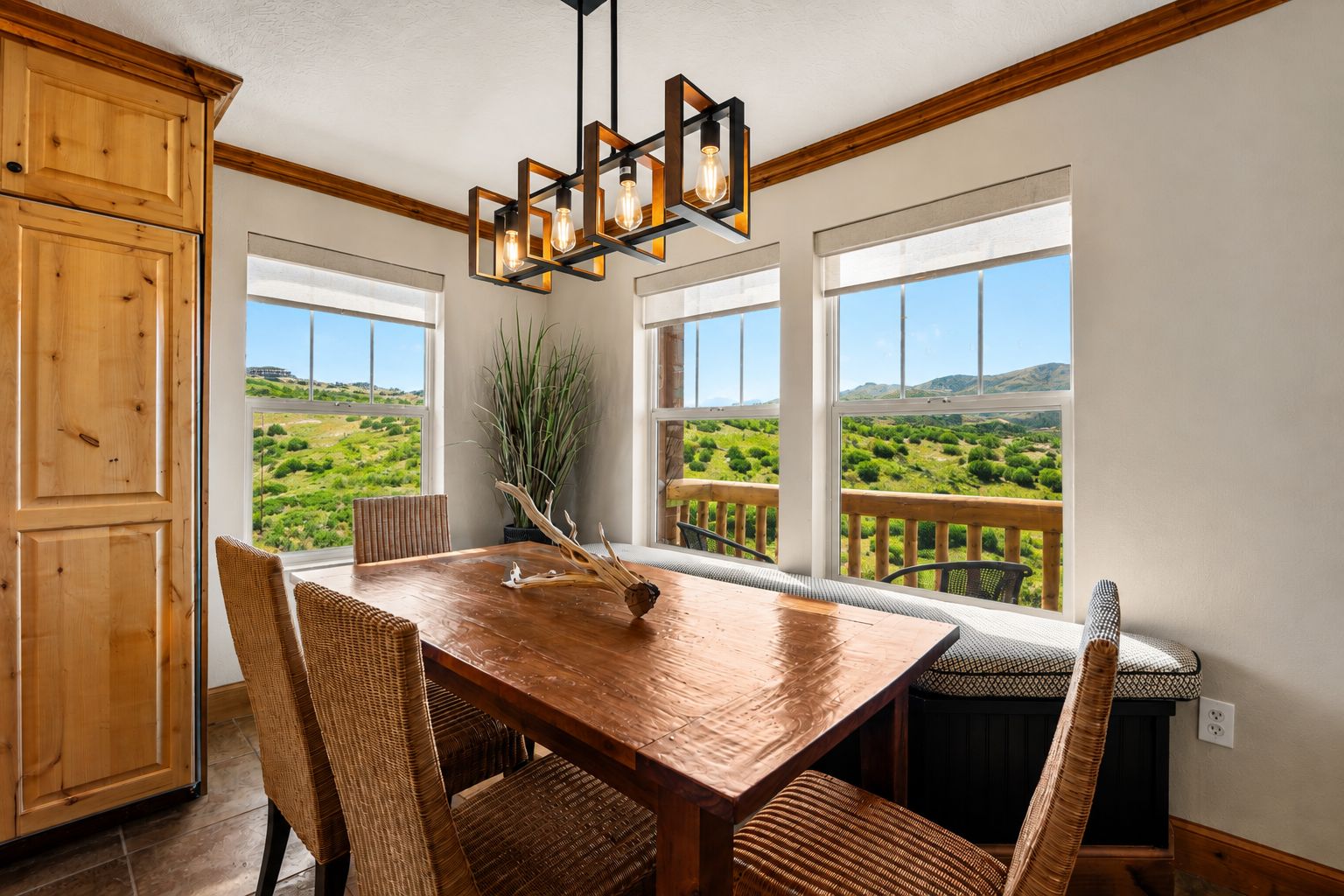 Un comedor con una mesa y sillas de madera, una lámpara colgante y vistas a un paisaje verde a través de amplios ventanales.