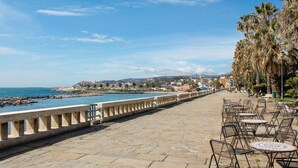 Un paseo marítimo con adoquinado de piedra, mesas al aire libre y palmeras.